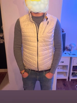 Vit dunväst från Parajumpers - Snygg vit dunväst från Parajumpers med quiltat mönster, hög krage och dragkedja framtill. Västen har en liten logotyp på nacken och praktisk ficka med dragkedja bak. Perfekt för lager-på-lager och stilren look. Passar perfekt för dig som är ca 170-178 cm lång