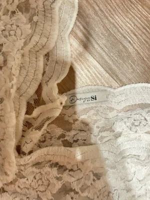 Vit spetsblus från Design by Si - Säljer en romantisk vit spetsblus från Design by Si. Blusen har v-ringning, korta ärmar och är helt täckt av blommig spets. Perfekt för dig som gillar feminina detaljer och vill ha en topp som sticker ut.