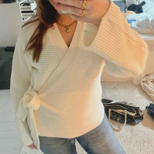 Krämvit omlottstickad tröja - Säljer en krämvit omlottstickad tröja från GinaTricot med breda ribbade ärmar och knytband i midjan. Har ändast provat den på, annars helt oanvänd!