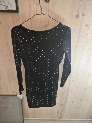 Svart sammetsklänning med pärlor - Snygg svart kortklänning i mjuk sammet med långa ärmar och pärlprydda detaljer över hela klänningen. Djupare ringning bak för en trendig look. Perfekt för dig som vill sticka ut lite extra.