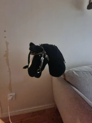 Svart käpphäst med träns - Säljer en svart käpphäst med vit bläs och flätad man. Hästen har ett brunt träns med silvriga detaljer och ringar. Perfekt för dig som gillar att leka häst eller vill ha en rolig leksak att rida runt på hemma.