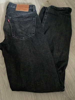 Svarta Levi's 501 jeans - Klassiska svarta Levi's 501 jeans med rak passform och femficksmodell. Jeansen har en vintage tvätt och den ikoniska röda Levi's-lappen på bakfickan samt läderpatch i midjan. Perfekta för en avslappnad och tidlös stil. Stl w28 l32. Helt oanvända, endast provade hemma. Hör av dig vid frågor! Pris kan diskuteras vid snabb affär!😊