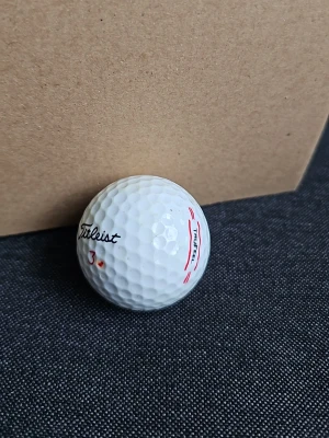Vit Titleist golfboll - En vit golfboll från Titleist med röd markering och siffran 3. Bollen har klassisk dimple-yta och märkning med svart och röd text. Perfekt för dig som gillar golf och vill ha en boll med bra känsla.