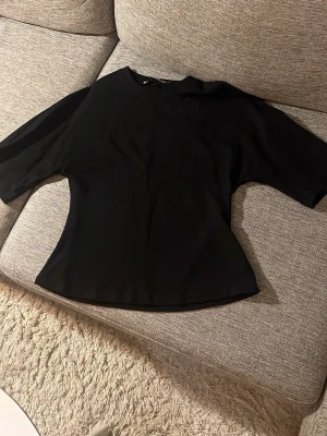 Svart enkel topp med kort ärm - En stilren svart topp med rund hals och korta ärmar. Modellen är lätt figursydd och passar perfekt till både jeans och kjol. Materialet känns mjukt och följsamt, vilket gör toppen bekväm att bära hela dagen.