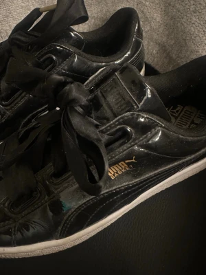 Svarta Puma Basket sneakers lack - Snygga svarta Puma Basket sneakers i glansigt lackmaterial med breda satinband som skosnören och vit sula. Guldiga Puma-loggor på sidan ger extra stilpoäng. Lite dammiga men tvättar självklart innan jag skickar! 