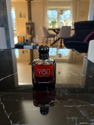 Stronger With You Absolutely parfym - En elegant parfymflaska från Emporio Armani, Stronger With You Absolutely. Flaskan är mörkbrun med svart rund kork och har en stilren, fyrkantig form. Perfekt för dig som gillar exklusiva dofter och snygg design på parfymhyllan.