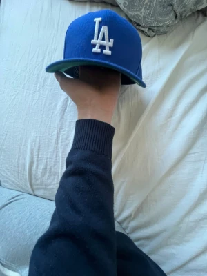 Blå LA Dodgers keps - Säljer en blå snapback keps från New Era med LA Dodgers-logga broderad i vitt framtill. Klassisk rak skärm och justerbar baksida. Perfekt för dig som gillar sportig streetstyle och vill ha en ikonisk look.