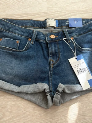  LTB jeansshorts low waist strl  NYA - Nya omvända Snygga blå denimshorts från LTB med klassisk femficksdesign och uppvikta benslut. Shortsen har low waist , knapp- och dragkedjestängning samt detaljer i kopparfärg. Perfekta för sommaren och lätta att matcha med olika stilar. 