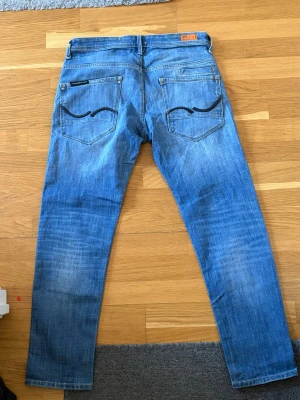 Blå jeans från Jack and Jones  - Säljer ett par klassiska blå jeans från Jack and Jones , Mike tapperd intelligens med raka ben och snygg slitning. Jeansen har fem fickor och ikoniska broderade detaljer på bakfickorna. Tillverkade i bomull för en skön och avslappnad känsla.