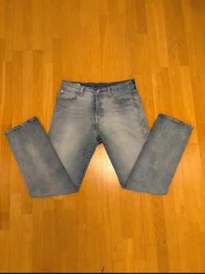 Ljusblå raka Levi's jeans (Real) - Säljer ett par klassiska ljusblå jeans från Levi's med rak passform och fem fickor. Jeansen har en snygg tvättad look och är tillverkade i slitstark denim. Perfekta för en avslappnad och trendig stil.