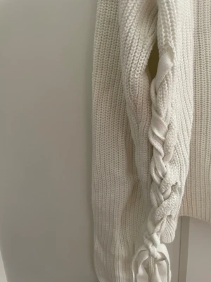 Vit stickad tröja med snörning - Trendig stickad tröja med ribbad struktur och snygga snörningsdetaljer längs båda sidorna. 