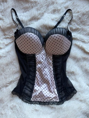 Svart och vit prickig korsett topp - Supersnygg korsett i svart och vitt med prickigt mönster framtill och vadderade kupor. Axelbanden är justerbara!! köpt second hand men den passade inte helt därför säljs den! i storlek S! köpt för 400 , nypris 200
