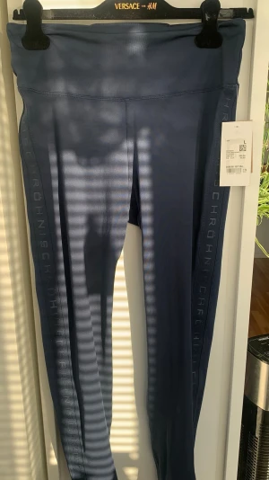 Blå träningstights från Röhnisch - Snygga blå tights från Röhnisch med hög midja och diskret logga längs benen. Tillverkade i ett stretchigt och mjukt material som sitter skönt på kroppen. Perfekta för träning eller chill dagar. Klassisk passform med långa ben.