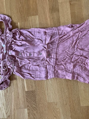 Rosa jumpsuit med knappar - Supersöt kortbenad jumpsuit med off shoulder-design och dekorativa knappar framtill. Den är från Kappahl i stl 152 men passar typ mig som har xs-s, det beror på hur man vill att den ska sitta. Måtten uppifrån och ner är 53 cm. Den är i bra skick kanske använd någon gång. Perfekt nu för sommaren! Stryker såklart innan frakt. Hör av er om frågor!💗(Säljer även på Vinted ifall man skulle vilja köpa där)
