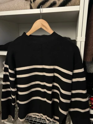 Svart stickad tröja med ränder Vero Moda - Snygg svart stickad tröja från Vero Moda med breda vita horisontella ränder. Tröjan har rund halsringning och långa ärmar.