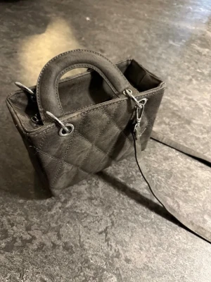 Svart axelremsväska i skinnimitation - Snygg svart handväska med lång axelrem och enkel design. Väskan är tillverkad i skinnimitation och har en stilren, rektangulär form. Perfekt för dig som gillar minimalistisk stil och vill ha en praktisk väska till vardagen.