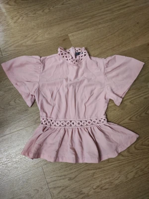 Ljusrosa blus med spetsdetaljer - ljusrosa blus med korta, vida ärmar och hög hals med spetsdetaljer.      Den är från shein.