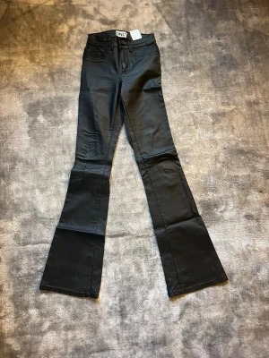 Svarta bootcut skinnbyxor från ONLY - Snygga svarta bootcut skinnbyxor från ONLY i storlek XS. Jeansen har normal midja, klassisk femficksdesign och utsvängda ben. Materialet har en lätt glansig finish som ger en trendig look. Perfekta för dig som vill ha en cool och modern stil.