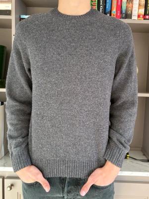 Uniqlo stickad tröja - Klassisk grå stickad tröja, från Uniqlo med rund hals och ribbade muddar vid ärmslut och nederkant. Tröjan har en enkel och stilren design, perfekt för lager på lager. Tröjan är något nopprig men väl omhändertagen.