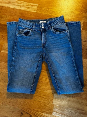 Blå jeans med små diamanter  - Säljer ett par blå midwaist bootcut jeans. Jeansen har dubbla knappar fram och bakfickor med små diamanter. Klassisk femficksmodell i stretchigt denimtyg för skön passform.