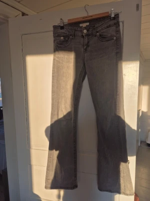 Grå bootcut jeans från gina tricot  - Säljer ett par grå bootcut jeans från gina tricot med klassisk femficksdesign och knappgylf. Jeansen har en snygg tvättad look och är tillverkade i mjukt denimtyg med lite stretch för extra komfort. Perfekta för dig som gillar en avslappnad men trendig stil.