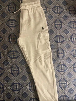 Vita mjukisbyxor från Polo Ralph Lauren - Snygga vita mjukisbyxor från Polo Ralph Lauren med broderad logga på benet. Byxorna har elastisk midja med dragsko och är gjorda i mjukt material som är perfekt för chill dagar. Klassisk och stilren design som är enkel att matcha.