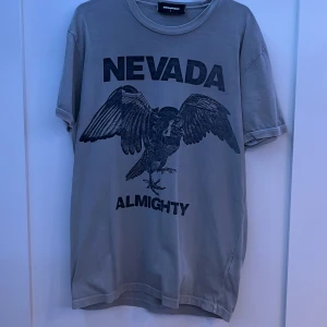 DSQUARED2 T shirt - Snygg grå t-shirt från DSQUARED2 med tryck av en örn och texten 'NEVADA ALMIGHTY'. Perfekt för en avslappnad stil med en cool vibe. Pris kan diskuteras!