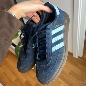 Blå Adidas Spezial sneakers - Snygga blå Adidas Spezial sneakers med ljusblå ränder och gummisula. Skorna har en klassisk design med snörning och är perfekta för en avslappnad stil. Har använt de max 5 ggr så är i fint skick och har mest stått o samlat lite damm. Säljer för att de inte kommer till användning. Passar mig oftast har storlek 39. 