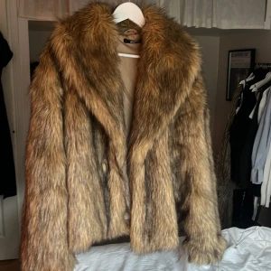 Brun pälsjacka från Gina Tricot - Säljer en snygg brun pälsjacka från Gina Tricot i storlek XL. Jackan har en lyxig look med sitt fluffiga material och är perfekt för att hålla värmen under kyliga dagar. Den har en klassisk design med långa ärmar och en mjuk känsla.