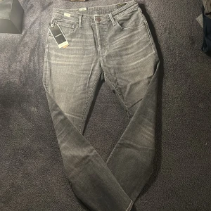 Grå jeans från Jack & Jones - Snygga grå jeans från Jack & Jones med en klassisk femficksdesign. De har en knappgylf och är tillverkade i ett bekvämt denimtyg. Perfekta för en stilren look. Endaste testade (slim straight) Storlek W33 L32. Pris kan diskuteras NYPRIS ~1000kr