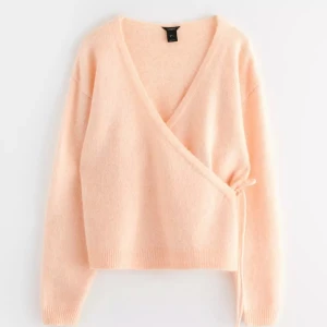 omlottkofta - Säljer en mjuk och stilren ljus korall/aprikos färgad omlottkofta med knytning i sidan. Koftan har långa ärmar och en v-ringad design som ger en elegant touch. Perfekt för att lägga till en färgklick i garderoben. Endast använd en 1 gång, så i nyskick endast lite nopprig (sista bild), storlek S.