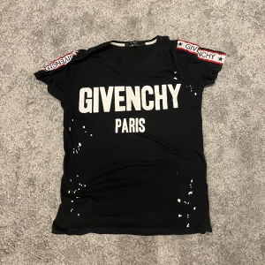 Svart t-shirt från Givenchy - Skick 8/10 | Snygg svart t-shirt från Givenchy med vit text 'GIVENCHY PARIS' på framsidan. T-shirten har korta ärmar med röd och vit detalj med stjärnor och Givenchy-logga. Perfekt för en stilren look | för frågor skriv!