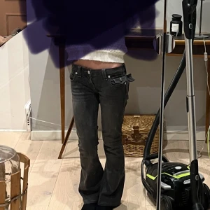 Svarta jeans från True Religion - Snygga svarta jeans från True Religion med låg midja och bootcut-stil. Byxorna har dekorativa fickor med knappar och märkets logga på baksidan. Perfekta för en trendig look. jag har sytt upp dom, skriv för fler bilder. 