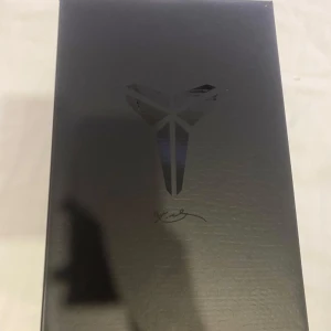 Svarta Kobes  sneakers med vit sula - Snygga svarta Nike sneakers med vit sula och vit swoosh-logga. Skorna har snörning och en låg profil, perfekt för en sportig look. De har en signaturdetalj på hälen och en mönstrad yttersula för bra grepp.