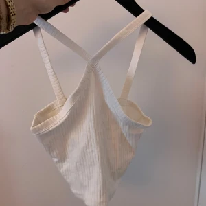 Vit ribbad linnetopp - Säljer en stilren vit ribbad linnetopp med smala axelband som korsas i fram. Från Gina tricot.