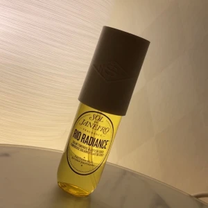 Sol de Janeiro Rio Radiance Parfym - Upptäck Sol de Janeiro Rio Radiance, en parfym med en solig doft som kombinerar rena vita blommor, krämig kokosmjölk och värmen av sand. Flaskan är genomskinlig med en gul nyans och har en stilren beige kork. Den är helt oanvänd!!