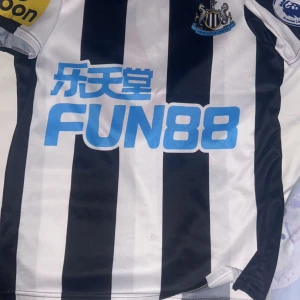 Svartvit randig fotbollströja - Säljer en svartvit randig fotbollströja från Puma med korta ärmar. Tröjan har sponsorlogga på framsidan och spelarens namn och nummer 'ISAK 14' på baksidan. Perfekt för fotbollsfans!