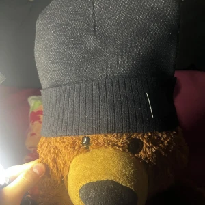 Svart stickad mössa - Snygg svart stickad mössa med ribbad kant och en liten svart etikett framtill. Perfekt för kyliga dagar och ger en stilren look.