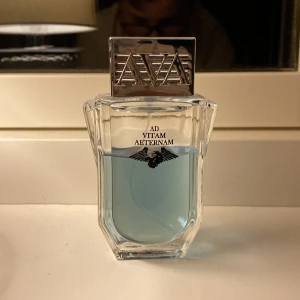 Ad Vitam Aeternam parfym - Säljer en elegant parfym med ljusblå vätska i en stilren, fyrkantig glasflaska. Flaskan har en silverfärgad kork med bokstäverna AVA ingraverade. Perfekt för den som söker en unik doftupplevelse. Boxen är tyvärr borta