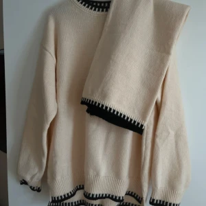 Beige stickad tröja med svarta detaljer - Helt nytt mysigt cremefärgat stickat set som jag fick i julklapp men som tyvärr inte passar mig.  Det är i strl L, byxorna går till anklarna på mig som är 168, se bild. Tröjan har en avslappnad fit och byxorna är superstretchiga vilket gör att de passar många olika storlekar!🧸 Priset är för båda delarna tillsammans. Köpt för 450kr