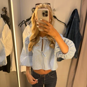 Randig blus med knytband - Säljer en söt blus med blå och vita ränder. Blusen har puffiga trekvartsärmar och ett knytband framåt. Perfekt för en somrig look! I nyskick ☺️