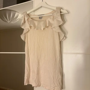 Beige topp med volangdetaljer - Säljer en söt beige topp med volangdetaljer runt halsen och axlarna. Hör av er vid funderingar eller om ni vill ha bilder med hur plagget sitter på mig. Titta gärna in mina andra plagg!