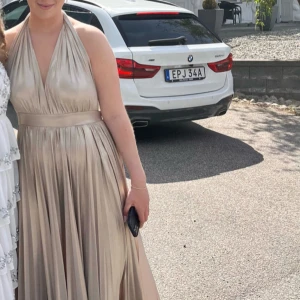 Champagnefärgad långklänning från bubbleroom - Elegant champagnefärgad långklänning med djup v-ringning. Perfekt för en festlig kväll eller bal. Storlek M. Knyt i nacken. 