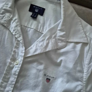 Vit skjorta Gant - Snygg vit skjorta från Gant med broderad logga på bröstet. Skjortan har långa ärmar och knappar framtill. Perfekt för en stilren look. Nypris 1399:-