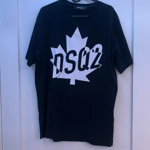Dsquared2 T shirt - Säljer en svart t-shirt från Dsquared2 med ett stort vitt lönnlöv och texten 'DSQ2' på framsidan. T-shirten har en rund hals och korta ärmar. Perfekt för en stilren look.