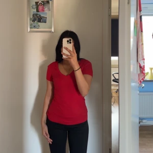 Röd v-ringad t-shirt från Tommy Hilfiger - Säljer en snygg röd t-shirt från Tommy Hilfiger med v-ringning. Perfekt för en casual look. Den har en liten logga på bröstet som ger en stilren touch. Storlek xxs men passar mig som har xs. Aldrig använd. 