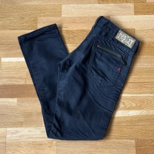 Dam Replay Shaula WV497 Svarta Jeans - Dam Replay jeans i modellen Shaula WV497 och färgen svart. OBS! Saknar mateall droppen som ska hänga från dragkedja på vänster bakficka! Syns på bild tre! Dragkedjan funkar fortfarande och går att dra i med draget! Storlek: 28 W, 30 L, Midja: 39.5 cm Ytterben: 92.5 cm Benöppning: 15 cm Material: 100% Cotton.