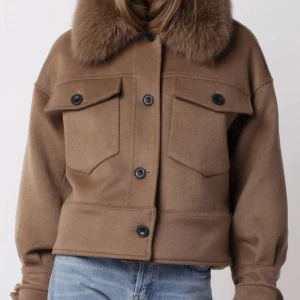 Brun jacka med pälskrage - Snygg brun jacka med en lyxig pälskrage och stora knappar framtill. Jackan har en croppad passform och två stora fickor med lock. Perfekt för att hålla stilen i kyligare väder. Fungerar till höst, vinter och vår. Har vanligtvis xs/s men denna passar perfekt!