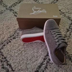 Grå sneakers från Christian Louboutin storlek 42 - Snygga grå sneakers från Christian Louboutin med den ikoniska röda sulan. Skorna har en stilren design med snörning och är tillverkade i mocka. Perfekta för den som vill ha en touch av lyx i vardagen. Insulan är 28 cm 