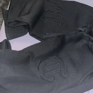 Svarta byxor med broderad logga - Snygga svarta byxor från Chrome Boys med en cool broderad logga på framsidan. De har en bekväm passform och är perfekta för en avslappnad stil. Shortsen har snörning i midjan för justerbar passform.